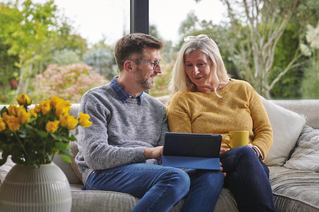 Couple sat on a sofa looking at an ipad.
