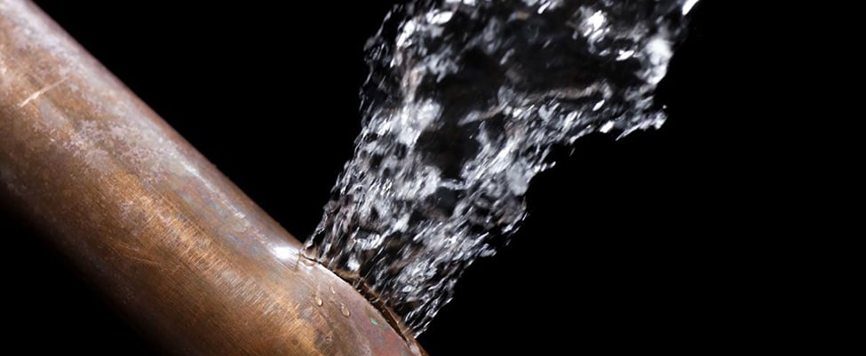 A close up of a burst copper pipe, with water spirting out.